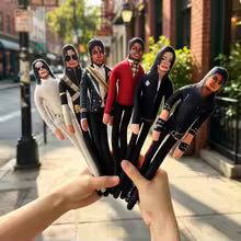 Six Michael Jackson doll figures in different outfits are held up by two hands against a blurred street background.
