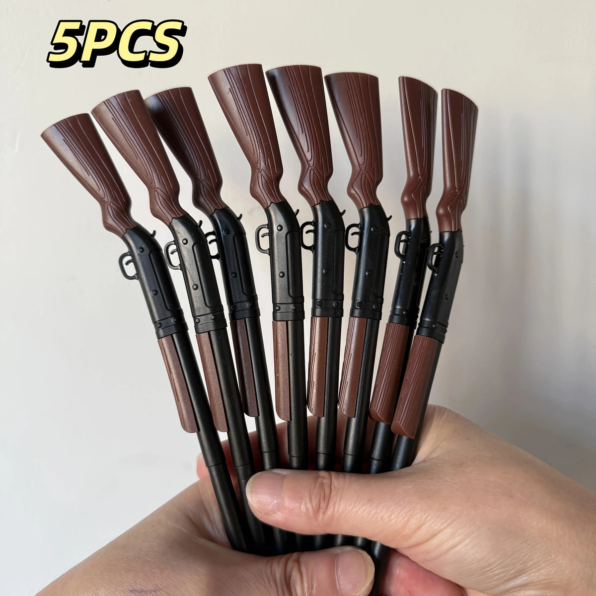 Five brown-and-black rifle-shaped ballpoint pens held in a hand